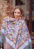 Woman wearing a pink and sky blue floral shawl with decorative patterns in an indoor setting.