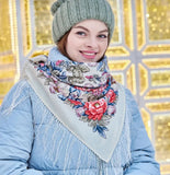 Woman wearing a floral Slavic scarf and green knit hat with a gold decorative background. Oversized winter palantine made of premium wool, showcasing intricate folk flower ornaments and fine ivory fringe borders.