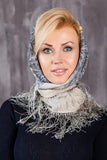 Woman wearing a decorative woolen beige headscarf in Slavic style against a gray background.
