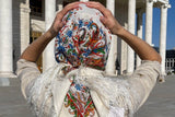 Person holding a colorful embroidered Slavic shawl in front of a classical building.