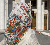 Person wearing a colorful embroidered ivory Slavic headscarf in front of a building with columns.