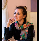 A beautiful ethnic Slavic shawl of 100% merino wool drapes over a woman’s shoulders. The natural sheep wool is adorned with pink flowers over a blue-gray base.