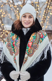 This Slavic-style 100% merino wool shawl is crafted from natural sheep wool. A woman wears the beautiful shawl decorated with a fine herbal pattern in red, yellow, and green on a white-red background.