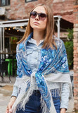 Woman wearing a blue lily patterned shawl outdoors with a brick building in the background. This milky white square shawl features light blue lilies and peony patterns for a gentle, classic style.