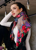 Woman wearing a colorful floral scarf with a black base. The shawl is made of merino wool. It is black and there are red roses in vintage style on it.