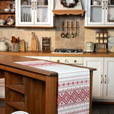 A white table runner with red geometric and traditional patterns draped over a wooden kitchen island in a real kitchen setting. 