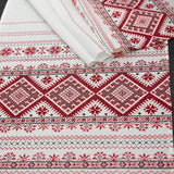 White fabric with red and dark gray traditional Slavic folk embroidery patterns, shown partially rolled out with a '100% cotton' badge overlay in the top right corner.