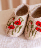 Pair of felted slippers indoor shoes with red poppy flower designs on a soft surface