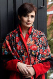 Woman wearing a colorful floral shawl with big vintage flowers. The base of the scarf is black and the peony flowers are red and beige. The material is wool.
