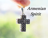 A silver bold square cross jewelry piece adorned with zircon stones, held in a person's hand.