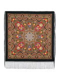 Decorative square shawl with intricate floral patterns and fringes on a black background. This black shawl features bold peony flowers in red and yellow with green leaves. A woman wearing it enjoys the soft merino wool, elegant style, and long black fringe.