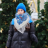 A woman wearing a beautiful Slavic ethnic shawl woven from 100% merino wool. The natural sheep wool features a gentle light blue herbal pattern on a milky white background.