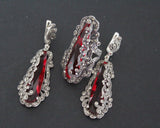 A luxury jewelry set featuring long drop earrings and a matching statement ring in 925 sterling silver. The design showcases elongated, faceted translucent red stones securely held within an intricate border of glittering marcasites. Handcrafted details include ornate vintage-style silver curls surrounding the central gems.