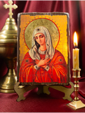 A religious Tenderness orthodox icon plaque of the Virgin Mary on a wooden stand, styled on a dark red fabric background with a brass chalice on the left and a lit candle on the right.