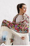 A woman wearing an oversized white merino scarf adorned with a vintage Slavic herbal pattern. The bright red and yellow peony flowers bring a retro folk charm, while the natural fabric and silky fringe add refined softness.
