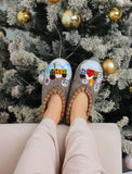 Gray merino wool slippers with festive winter designs worn by a person in front of a decorated Christmas tree.