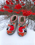 Gray woolen clogs slippers with red rowanberry and bullfinch bird embroidery on a snow with berries tree in the back.