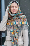 A woman wearing a brown, mint, and turquoise geometric patterned scarf with silky fringe.