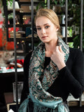 Woman wearing a patterned scarf in an indoor setting. This green paisley scarf with teal and black details has a soft, elegant look. The ethnic design is traditional and balanced, and the large size allows easy wrapping.