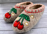Pair of felted woolen slippers with red cherry design on a wooden surface