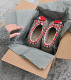Pair of gray woolen slippers with red accents in a cardboard box on a gray surface.
