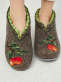 A pair of brown felt clog slippers with green trim and embroidered red apples with green leaves, shown on feet against a light gray background.