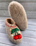 Pair of felted natural woolen slippers with cherry design on a wooden surface