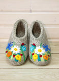 Pair of gray woolen slippers with floral embroidery on a wooden surface