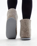 Brown slippers made of 100% wool with gray soles worn by a person on a white background