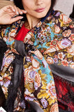 A woman wearing an authentic merino wool shawl cashmere like in deep brown, decorated with beige and navy blue ornaments and flowers. The silky fringe adds a luxurious touch, making this warm shawl a standout piece for refined, classic wardrobes.