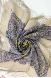 Paisley patterned beige scarf with fringes on a neutral background with yellow and gray details. 