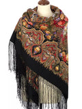 Decorative shawl with intricate patterns and fringes on a mannequin against a white background. A woman wearing this large black shawl looks refined and stylish. The large peony floral design stands out beautifully, finished with black fringe and made from soft merino wool.