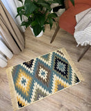 Decorative yellow and green rug with geometric pattern on a wooden floor, next to a plant and chair.