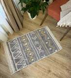 Gray patterned gray modern rug on a wooden floor with a plant and chair in the background
