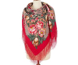 Red floral patterned merino wool women`s scarf with fringes on a mannequin against a white background. Close-up detail of a mannequin showcasing a luxurious Slavic-style red merino wool palantine. The oversized shawl features detailed botanical and paisley scrollwork over a multicolored base, with a highly textured, flowing red fringe hanging down.