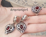 A photo showing a hand palm and a jewelry set on it in a shape of pomegranate silver oxidized earrings and ring. In the center of the pomegranate is a red cabochon garnet.