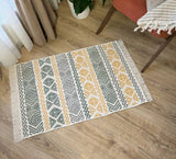 Patterned yellow and beige rug on a wooden floor with a chair and plant in the background