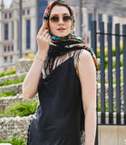 A woman beautifully draped in a large vintage merino wool winter shawl around her head and neck, showcasing intricate colorful peonies and field flowers with a long black fringe at the hem for a cozy wrap.