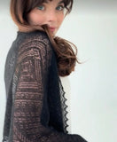 Delicate organic goat wool pashmina in black, handwoven into a sheer, thin lace pattern on a woman`s shoulders.