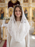 A woman wearing a white lace bridal veil over a cream-colored dress, standing in a brightly lit church interior with ornate gold and red architectural details in the background.