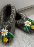 Pair of gray slippers with floral designs on a light wooden floor.