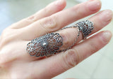 A hand wearing an adjustable double silver ring with a intricate spider net design.