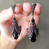 A pair of silver earrings featuring black onyx and marcasite details, displayed against a dark background.