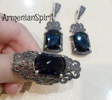 A navy blue stone ring and earrings set with silver marcasite details, held in a person's hand.