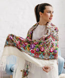 A woman wearing a white and pink floral patterned scarf with fringe, draped around her neck and shoulders.