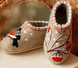 Elegant display of premium beige wool felt slippers with a clean, bootie style silhouette and a flexible rubber felt bottom. The rich crimson bullfinch and rowanberry embroidery stands out boldly against the matte white background of the natural sheep wool material.
