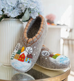 Pair of gray woolen slippers with winter scene design on a reflective surface.