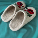 A pair of high-quality organic wool slippers in a soft ivory white shade, neatly arranged on a clean backdrop. The slippers feature matching asymmetrical botanical embroidery of rich crimson poppy blossoms with detailed dark shading on the front toe box.