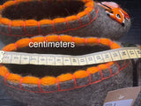 Felted felted warm slip on slippers with orange accents and a ruler for scale on a dark background
