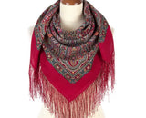 Red scarf with intricate pattern and fringes on a mannequin against a white background. The material features a solid, vibrant red background heavily decorated with large vintage ornaments in shades of soft pink and orange colors, framed by complex multicolored paisley and scrollwork patterns.